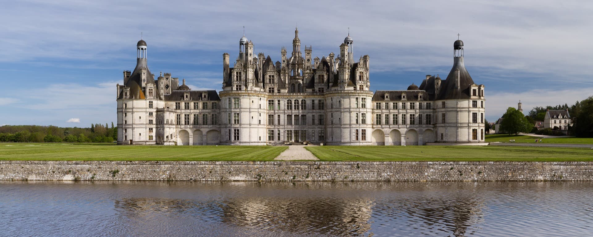 La façade nord-ouest de Chambord au crépuscule, sa forêt de tours et de cheminées se détachant sur un ciel dégagé.